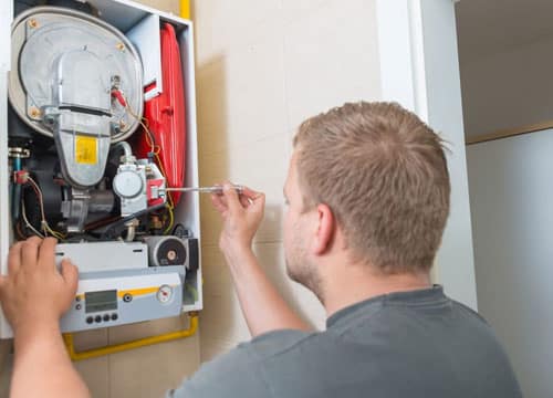 Man holding a small screwdriver to a boiler's check valve.