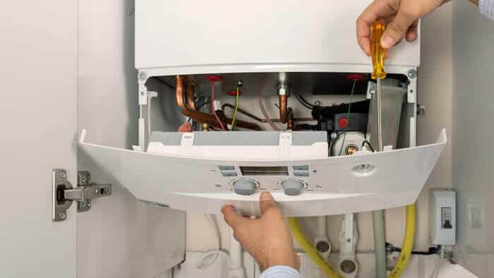 A man holding a heating door open with his left hand while holding a screwdriver in his right hand. He appears to be tightening a screw.