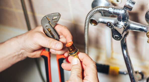 A man holding a wrench in his left hand and a valve in his right hand.